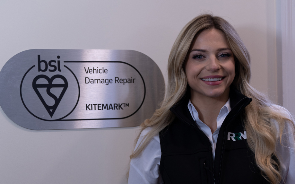 Alex Gray standing next to bsi Vehicle Damage Repair Logo on wall