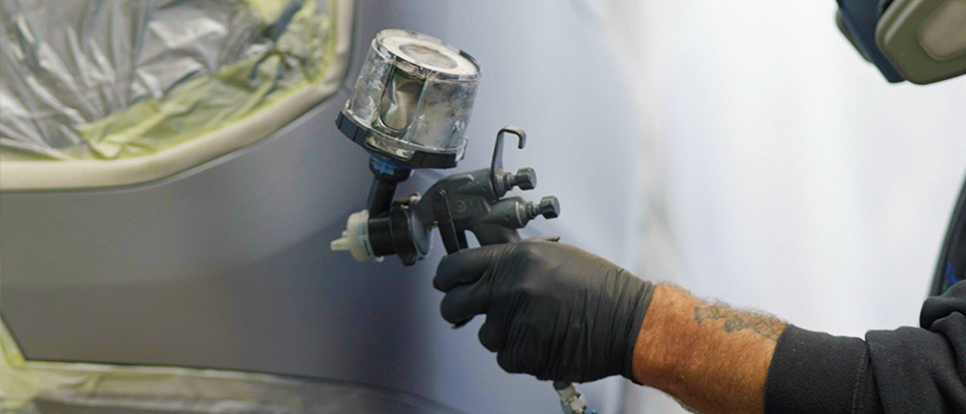 Cost-Effective Repairs Close up image of technician spray painting panel of car whilst wearing mask