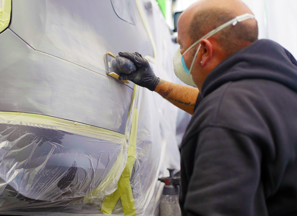 rrn_mobile-car-wing-dent Technician sanding car panel whilst wearing face mask